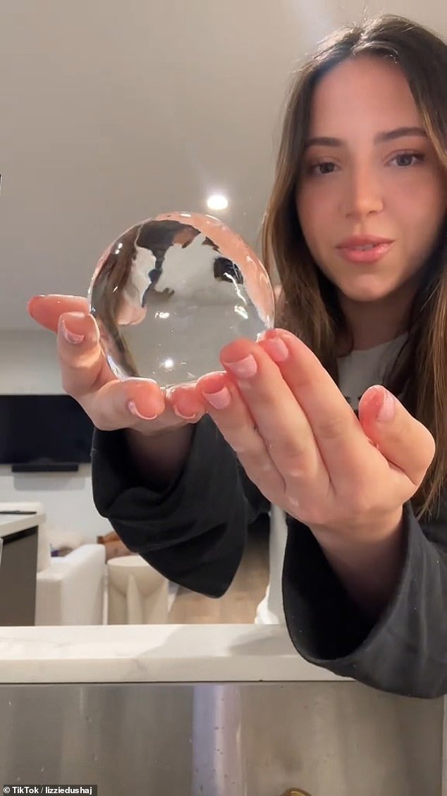 She takes the 'high quality water' ball and drops it into her 'low quality' water to check if it becomes crystal clear.  After a few seconds, Dushaj takes out the ice ball and marvels that it has become completely clear