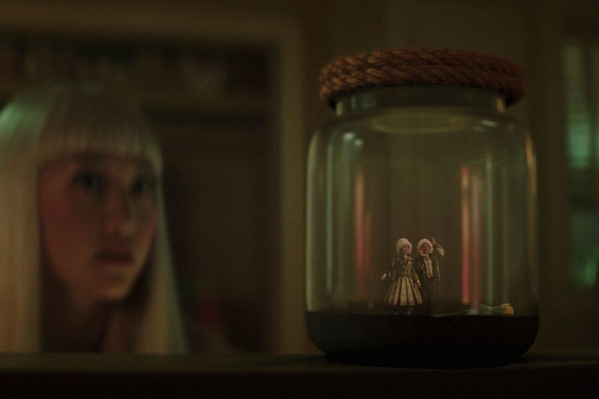 A girl looks at a jar containing two small sprites
