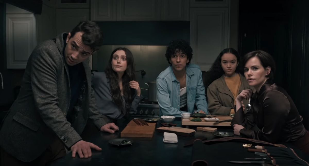 A group of worried-looking men and women sit at the end of a kitchen island.